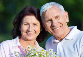Smiling older man and woman outdoors holding flowers