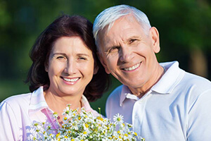 Smiling man and woman outdoors holding flowers