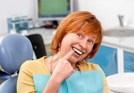 Senior woman in dental chair pointing to smile